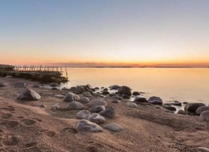 A sandy beach with stones on it and a dock at the background