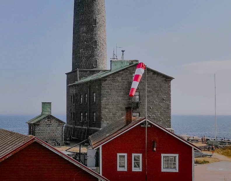 A lighthouse with surrounding read wooden cottages by the sea