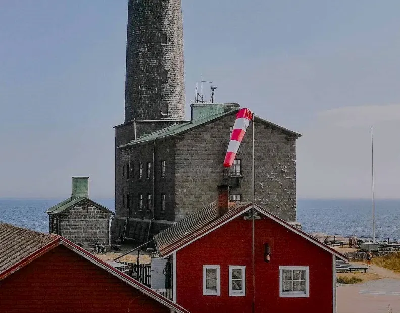 A lighthouse with surrounding read wooden cottages by the sea