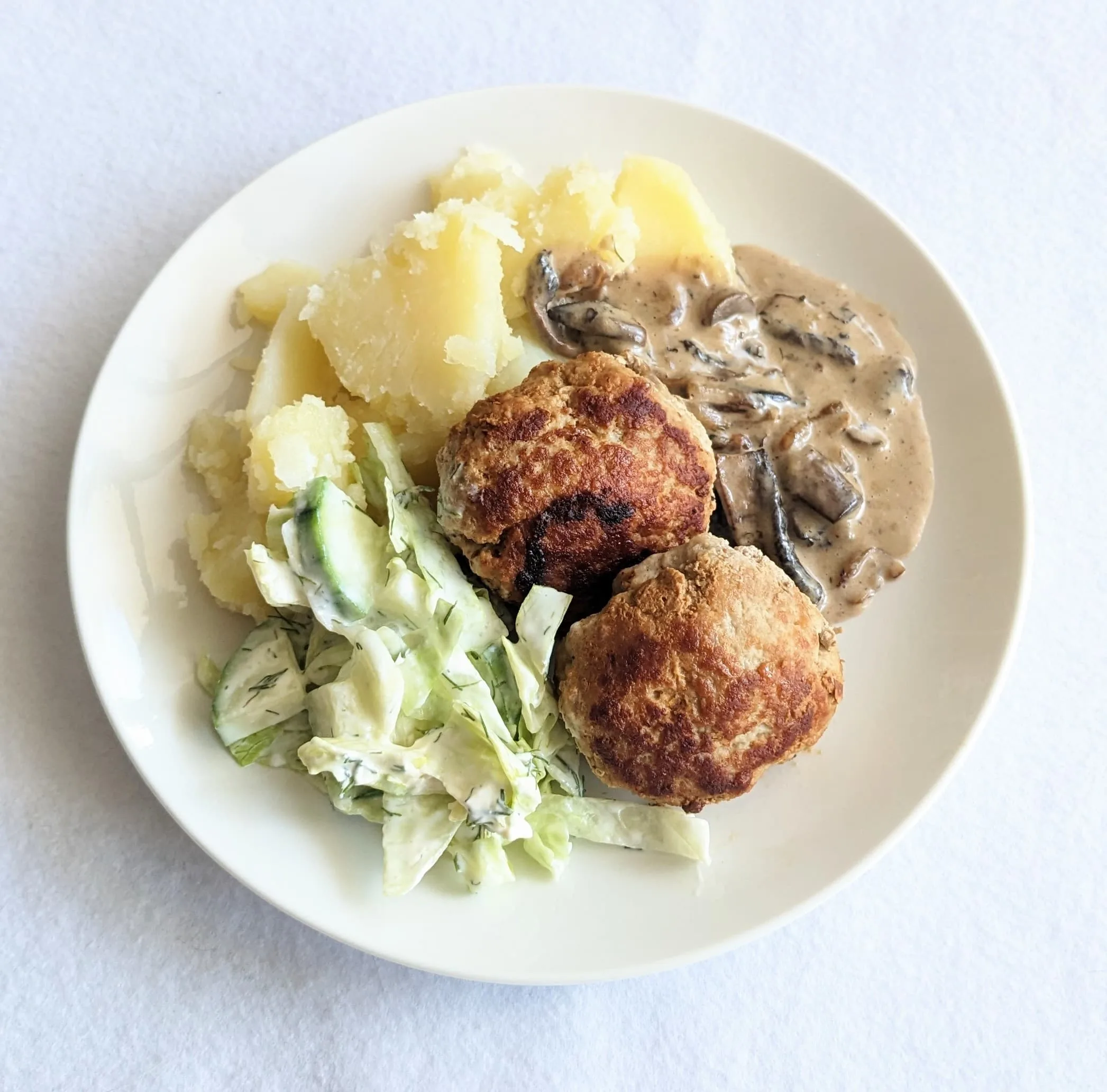 a white plate containing kotletes a latvian meat patty served with cabbage boiled potatoes and mushroom sauce