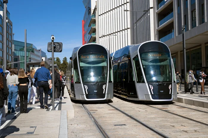 people waiting at a tram stop with two trams stationary in luxembourg city