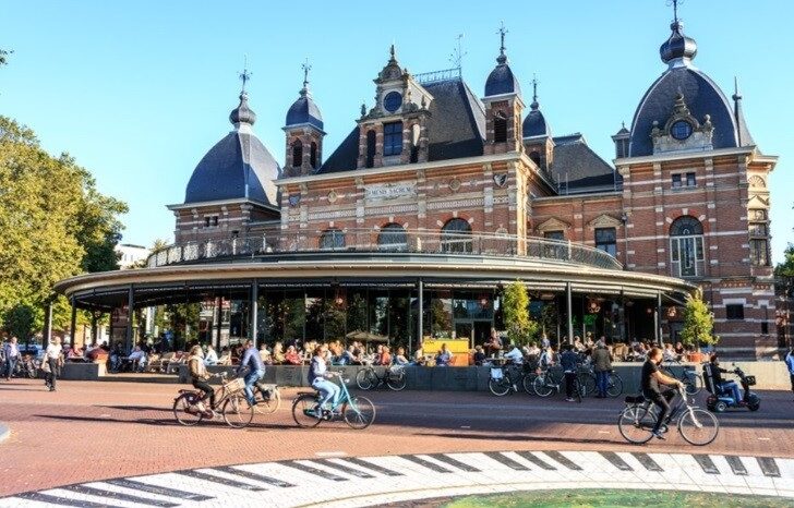 A view of Arnhem street with people riding their bicycles and a historic building in the background