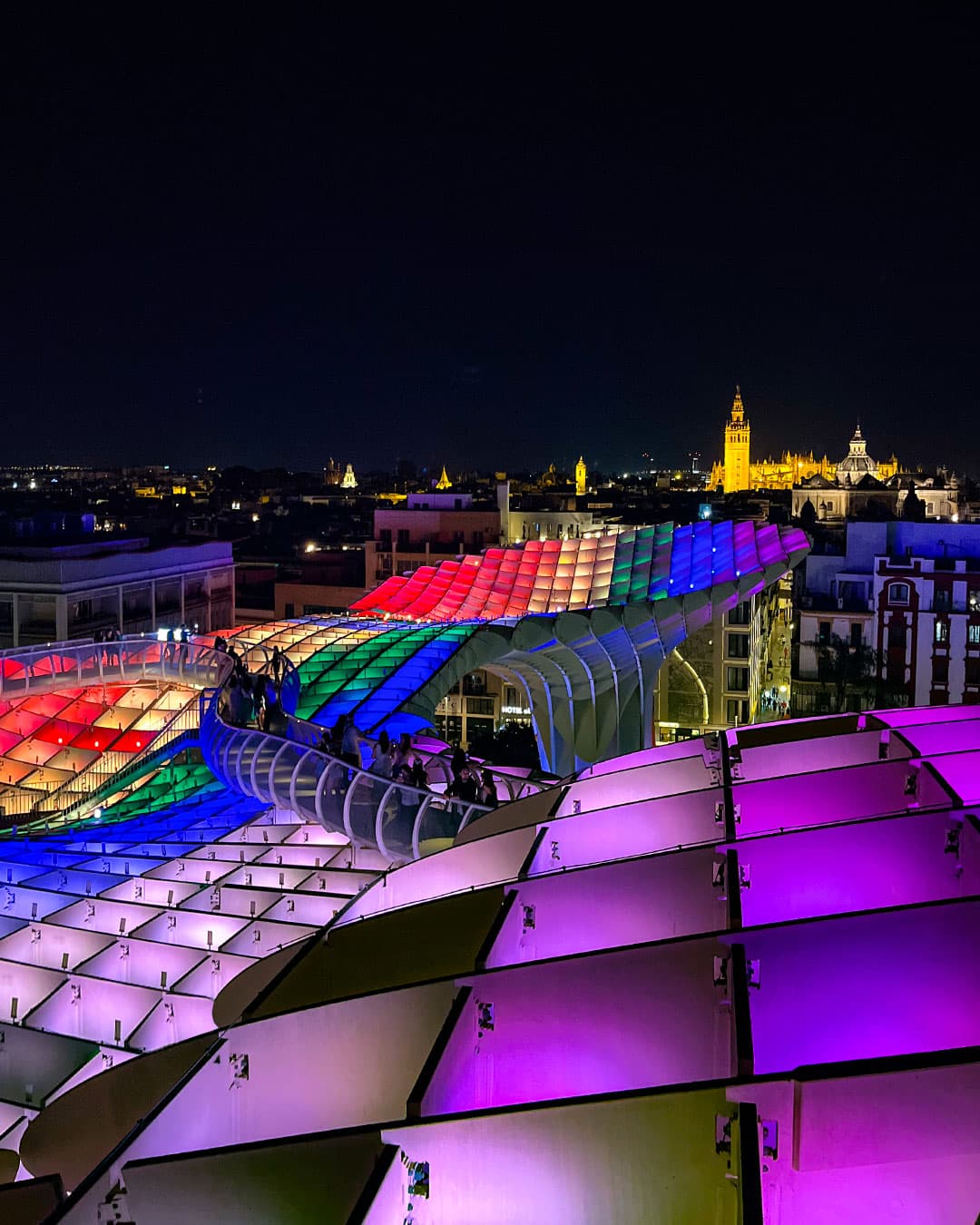 The Setas de Sevilla lit up at night in colours of the rainbow flag signifying Seville's all encompassing culture