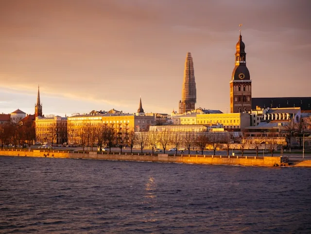 modern concrete buildings with the old town in the background sit behind the daugava river in riga latvia