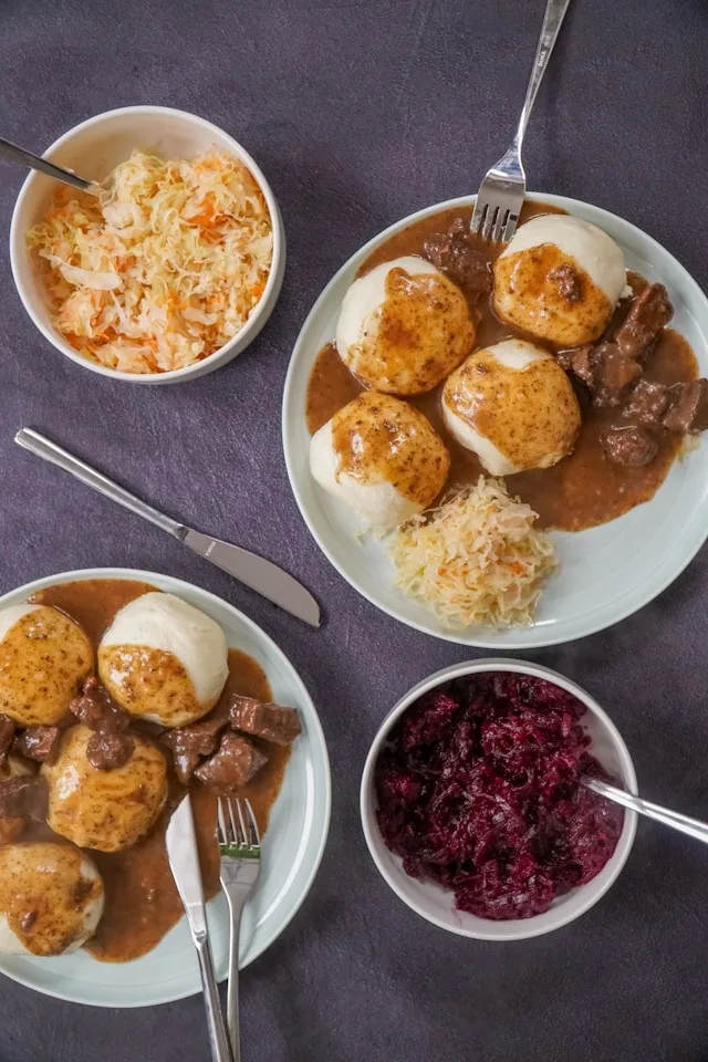 two plates of goulash with mashed potatoes and salad on a blue tablecloth