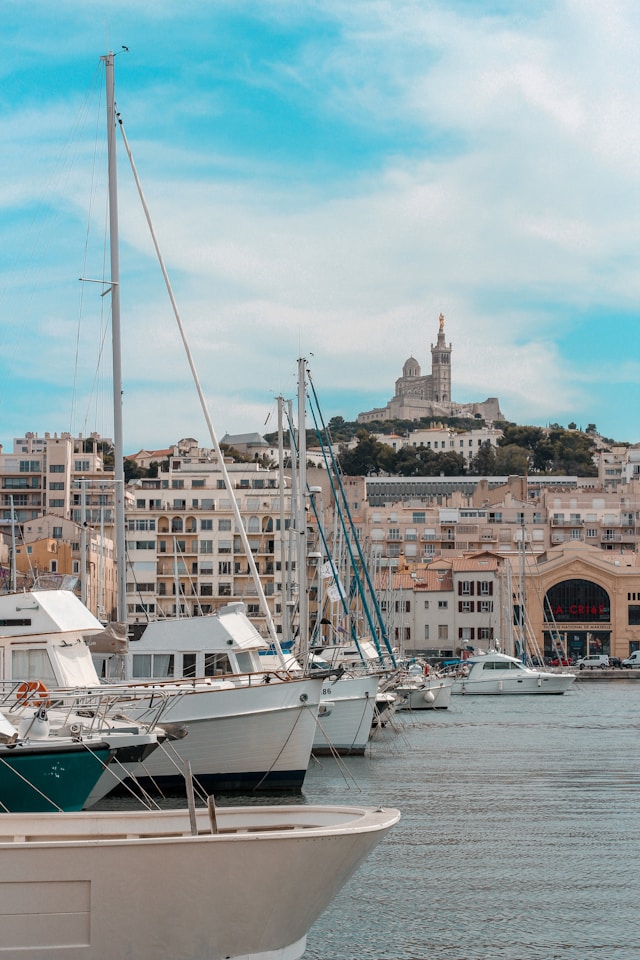 yachts moored in a harbor in marseille france with a church on a hillside in the background