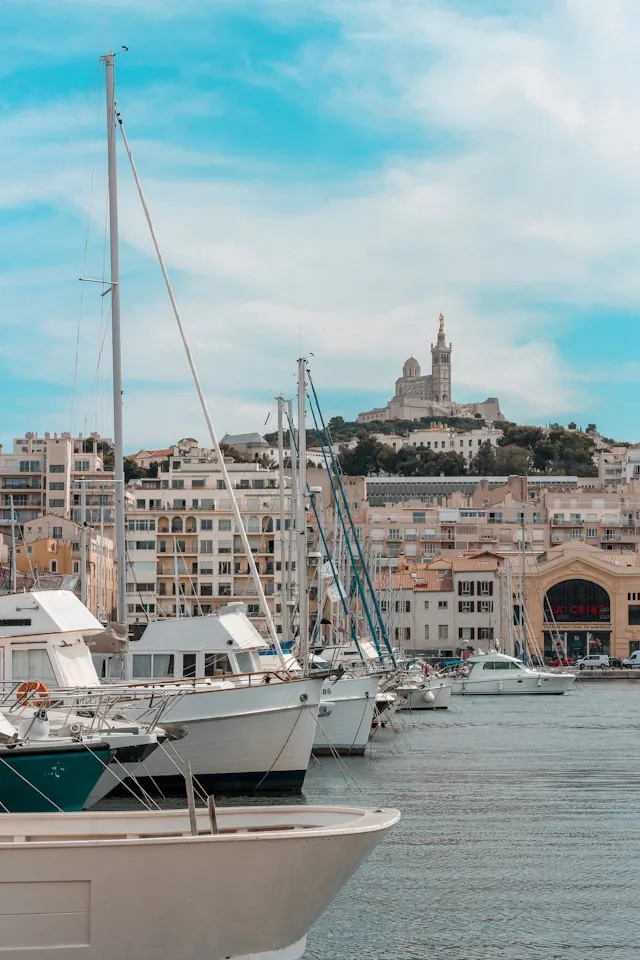 yachts moored in a harbor in marseille france with a church on a hillside in the background