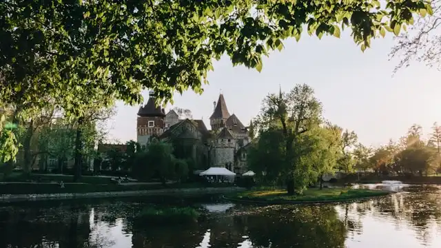 vajdahunyad castle covered by trees behind a lake in budapest hungary