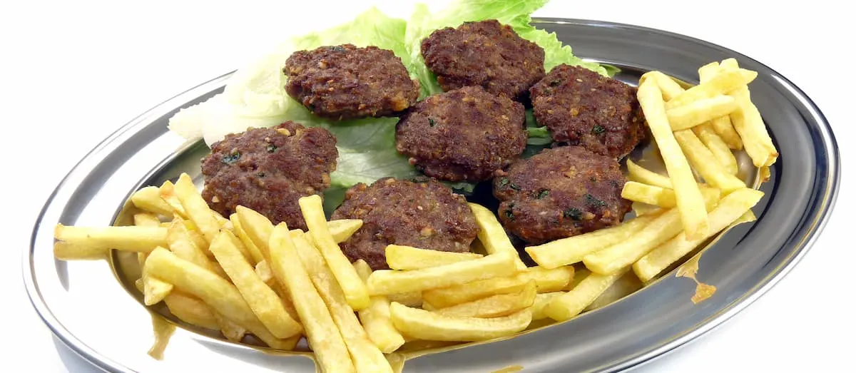 a metal tray with french fries and albanian qofta on top of a salad garnish