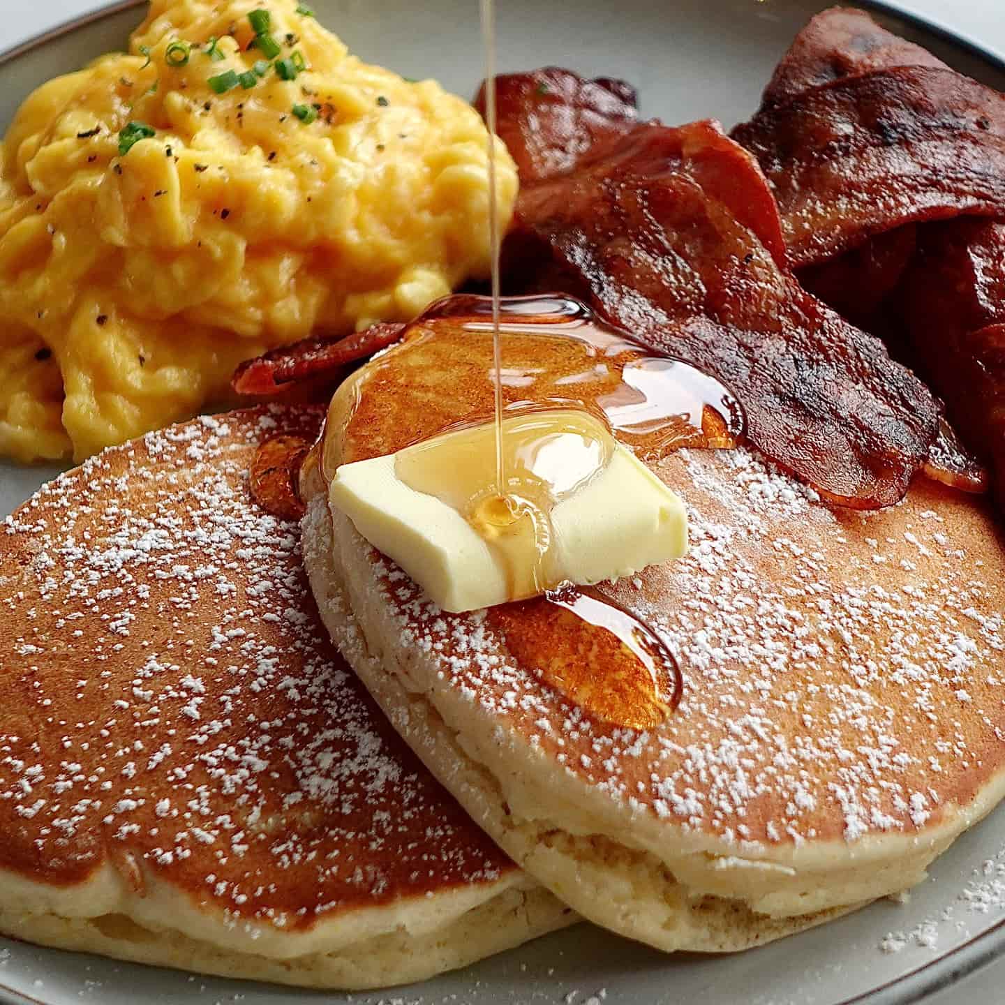 Pancakes, crispy bacon, syrup and scrambled eggs
