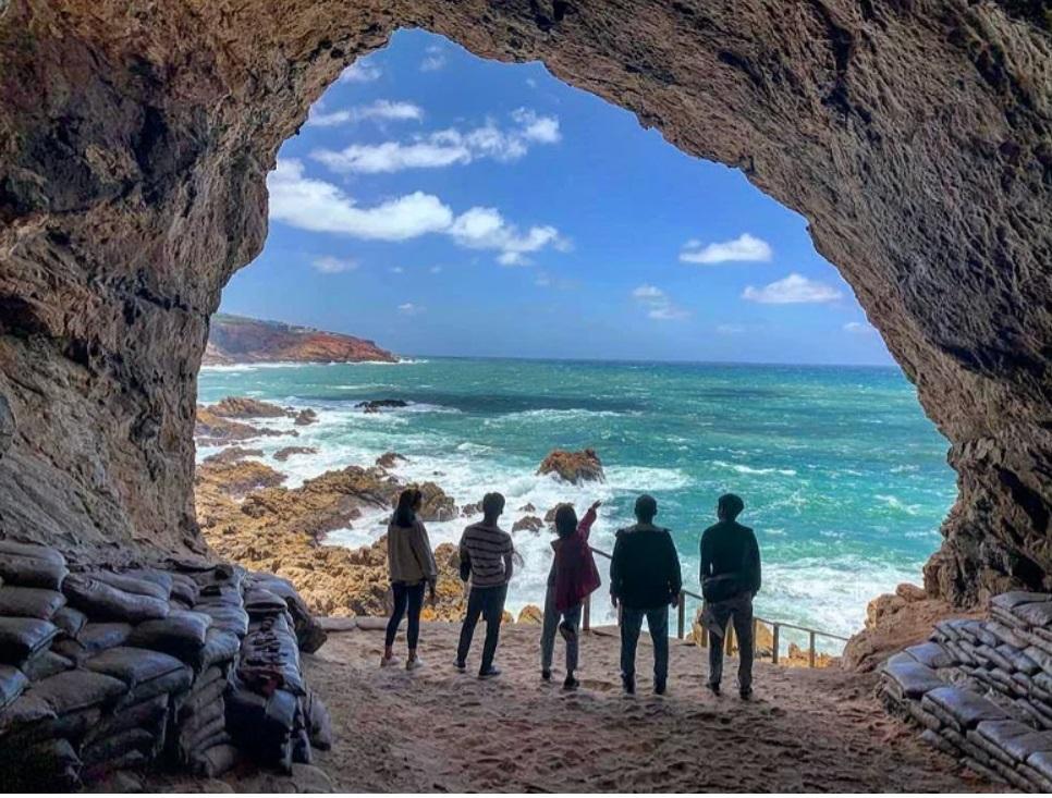 Humans standing at the mouth of a cave, overlooking a blue ocean