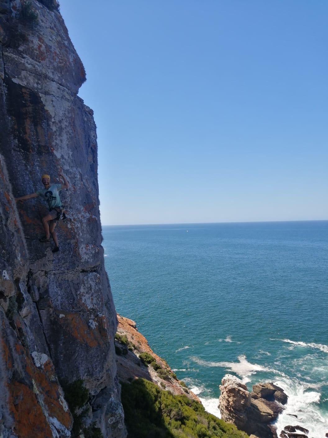 A climber on a rock wall above a blue ocean