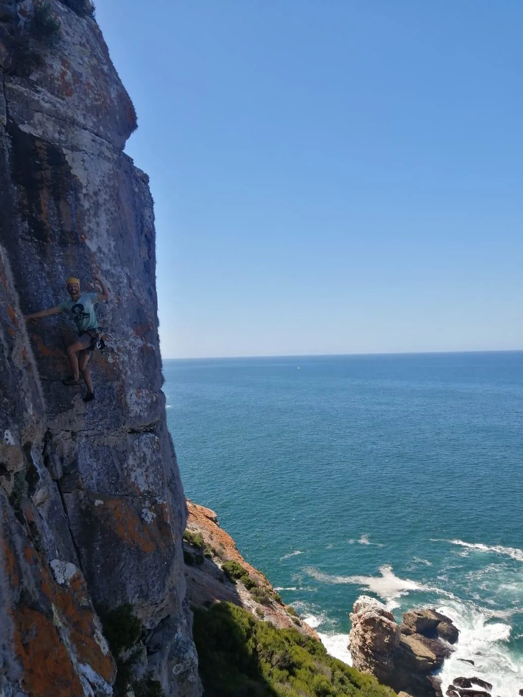 A climber on a rock wall above a blue ocean