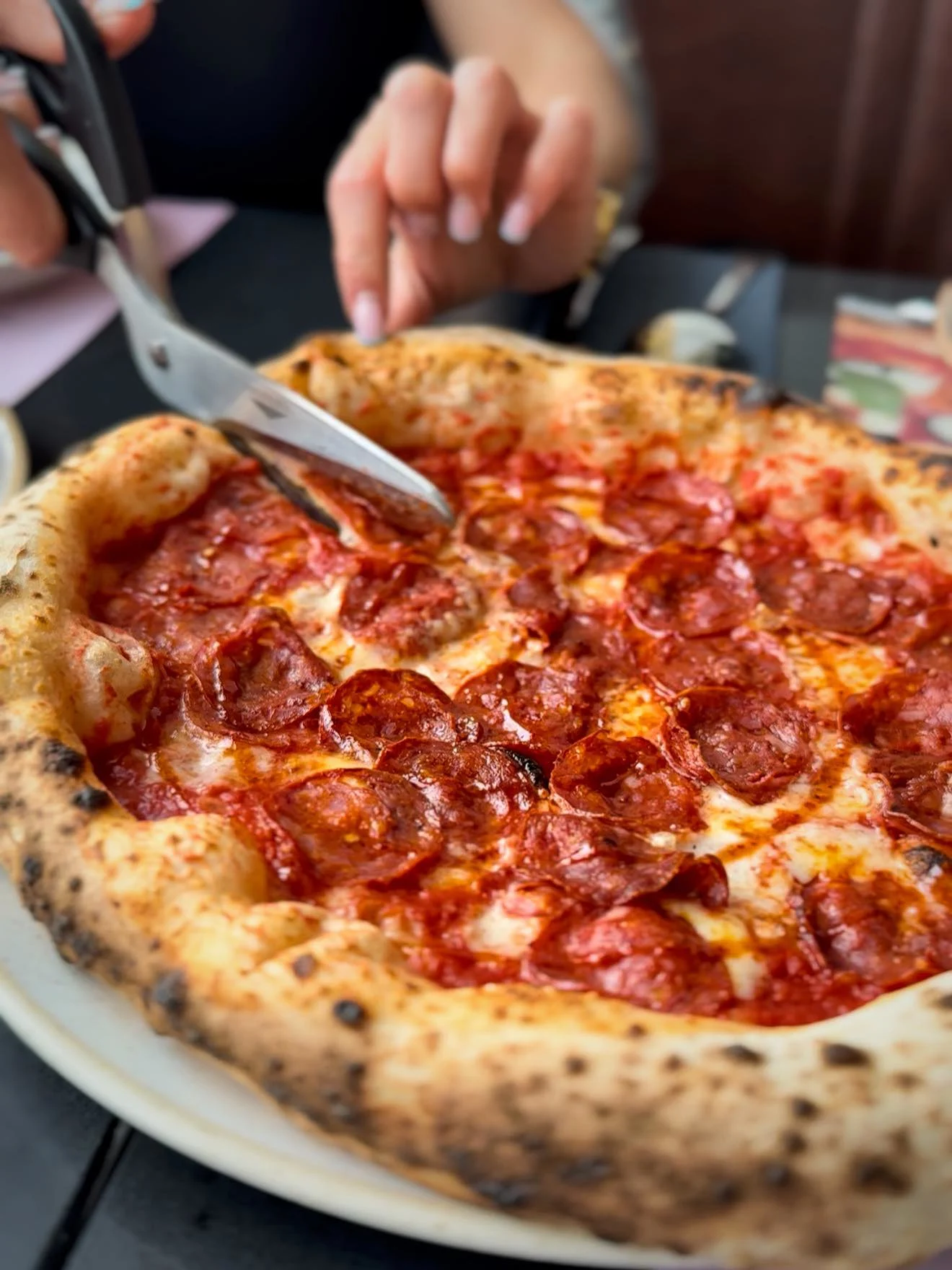 a chef cuts a neapolitan pepperoni pizza with scissors at OSTRO restaurant in gdansk poland