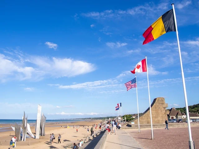 german, canadian and u.s. flags fly above a d-day memorial on a beach in northern france