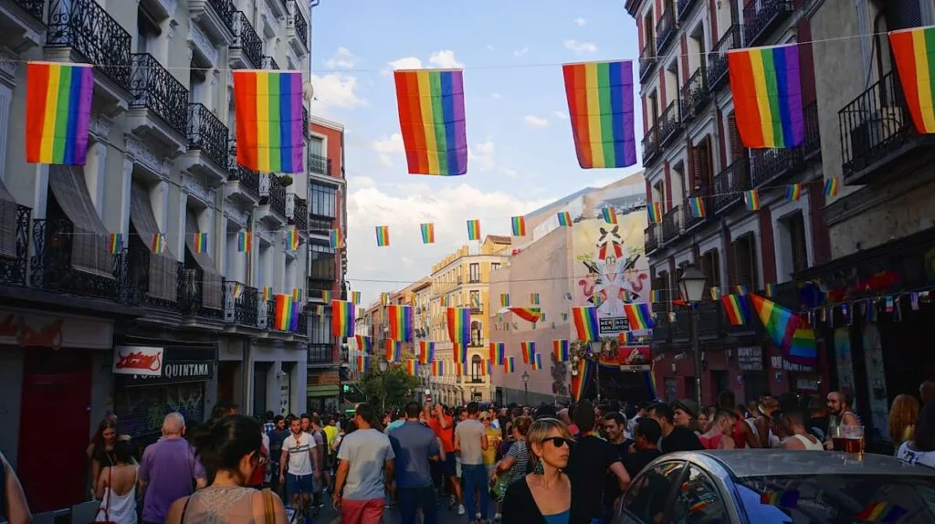 a crowd walks below rainbow flags in chueca madrid spain