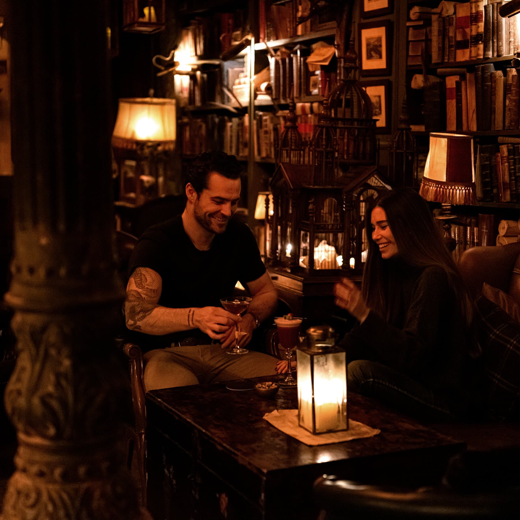 a man with a tatooed arm and a woman drink cocktails in jack's  library speakeasy bar in madrid spain