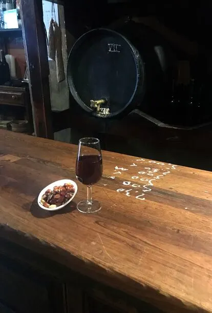 a glass of sherry and a bowl of nuts on a wooden table at la venencia one of the best bars in madrid spain
