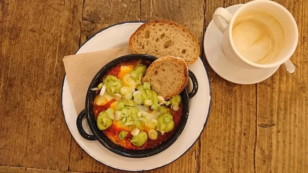 a plate of baked eggs topped with spring onions and a coffee on the side from plenti a british cafe in madrid spain