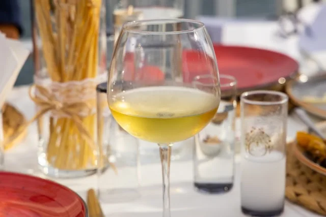 a glass of spanish white wine on a table with breadsticks in the background