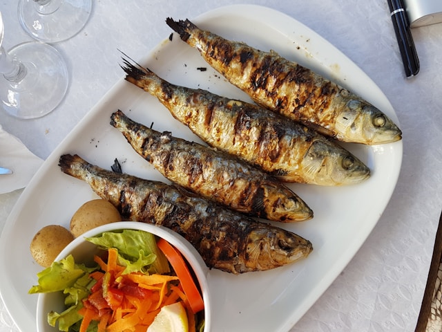 a plate of grilled sardines with salad in a bowl
