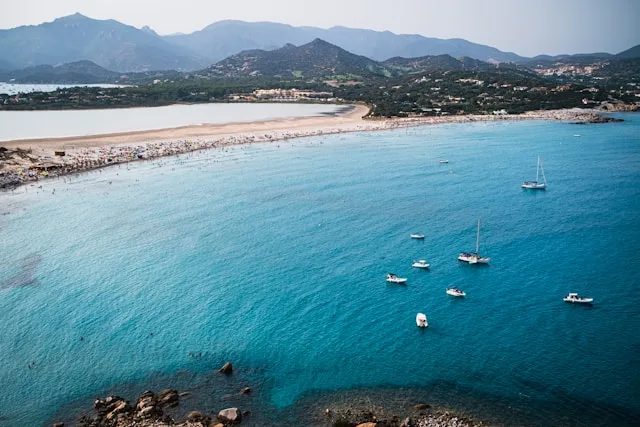 a tombolo beach with mountains in the background and yachts in the foreground in villasimius sardinia italy