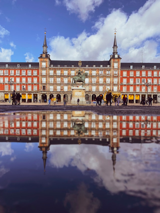 a statue of king phillip iii in plaza mayor madrid spain with buildings in the background and reflections in a body of water in the foreground