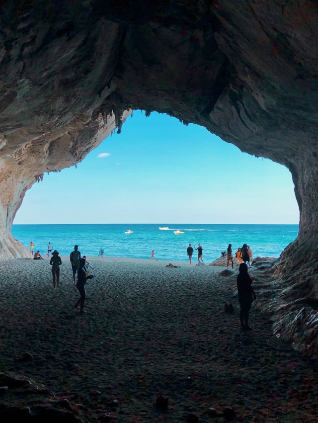people standing on a pebble beach at the mouth of a cave in sardinia italy