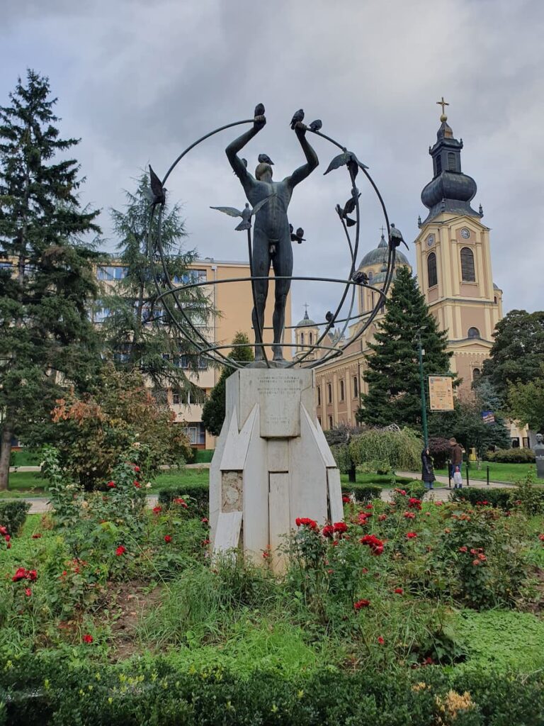 a statue in central park with a cathedral in the background in sarajevo bosnia