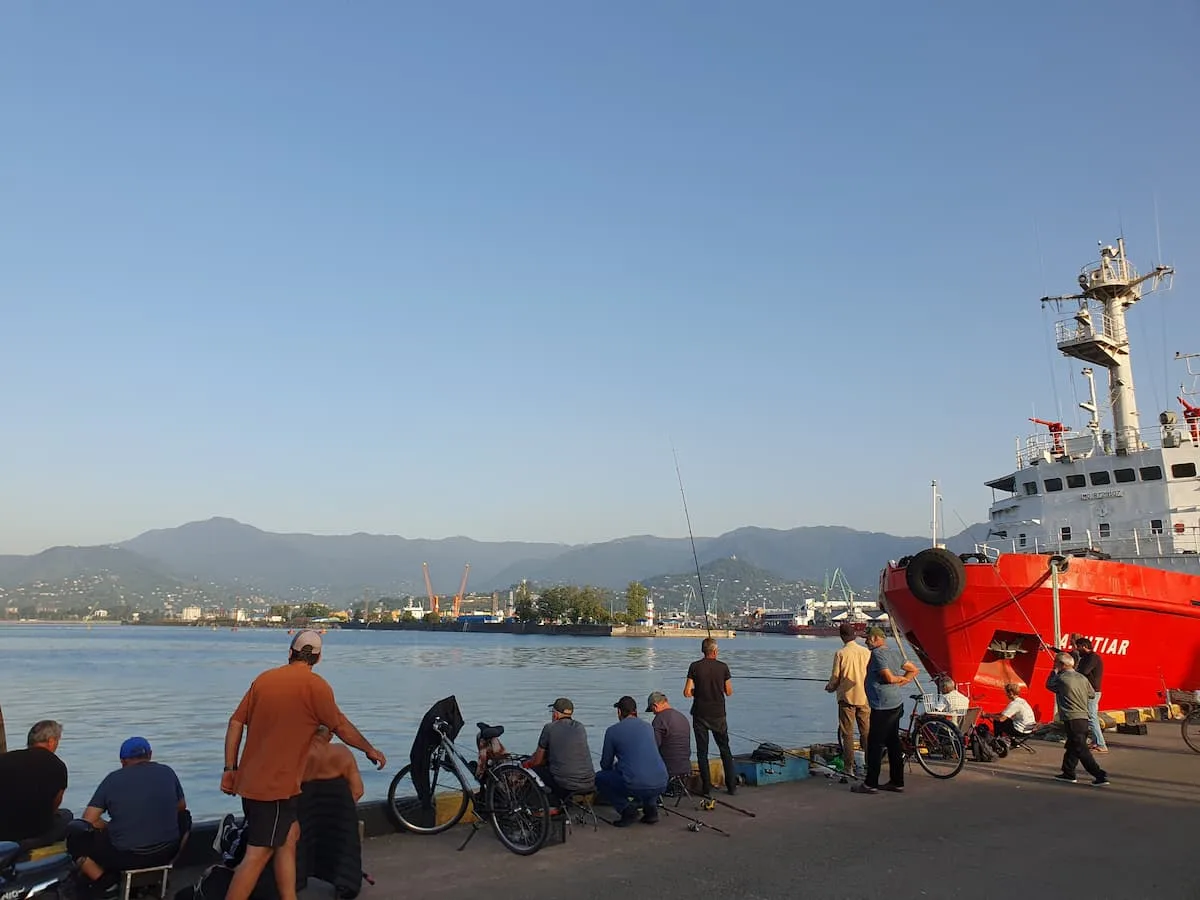 fisherman and a red boat at the port of batumi georgia with the adjaran mountains in the background