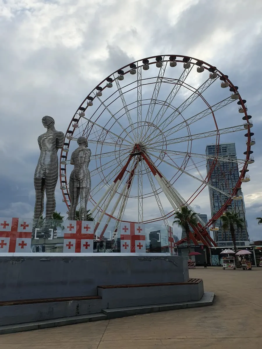 a statue of ali and nino with a ferris wheel in the background in batumi georgia