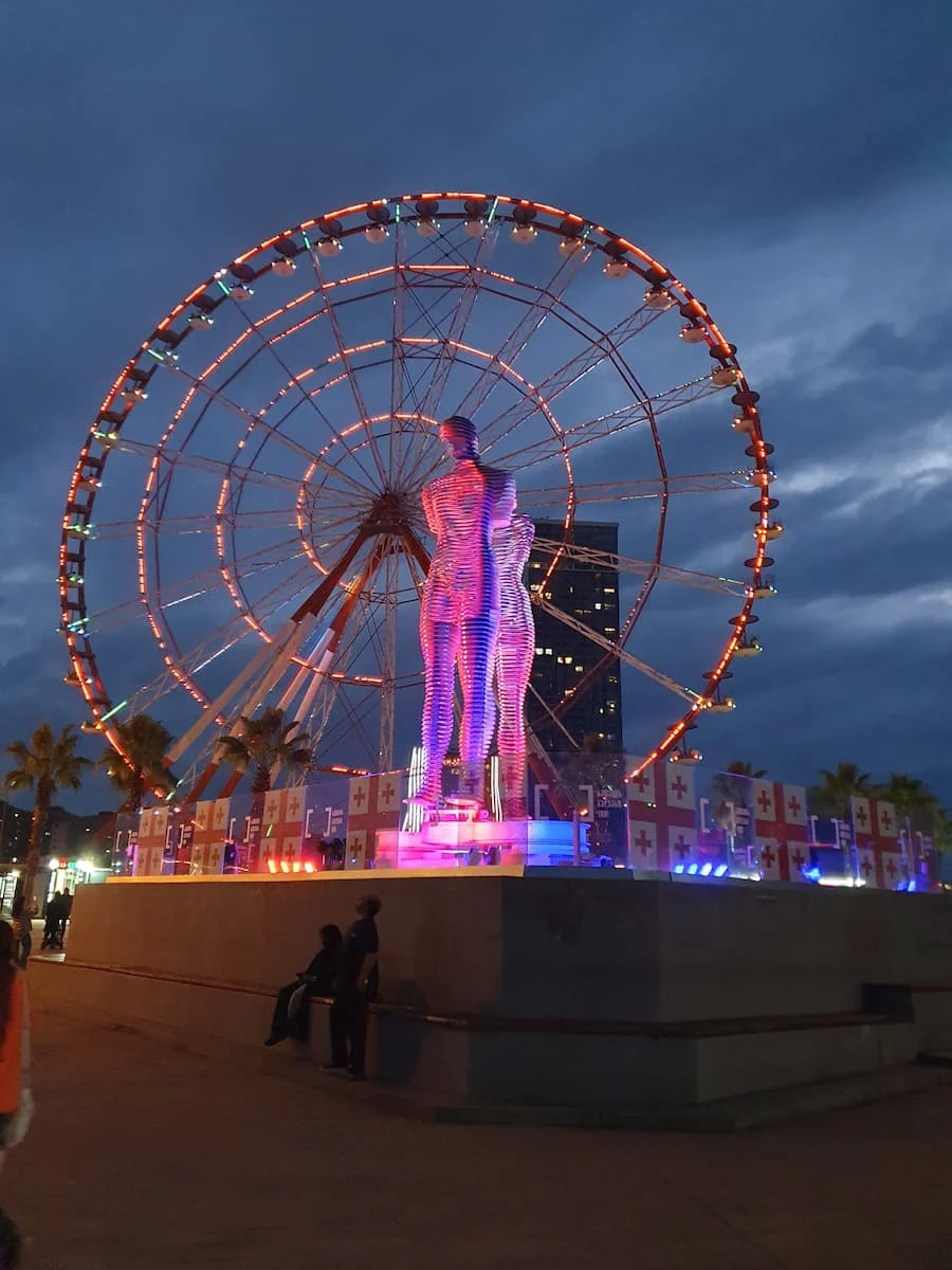 an illuminated statue of ali and nino in front of a ferris wheel at night in batumi georgia