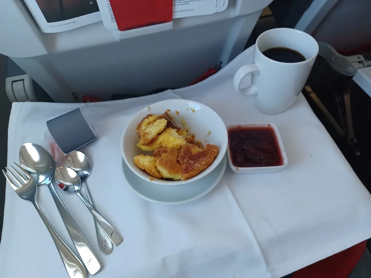 a bowl containing kaiserschmarrn with metal cutlery and a mug of coffee on a white tablecloth