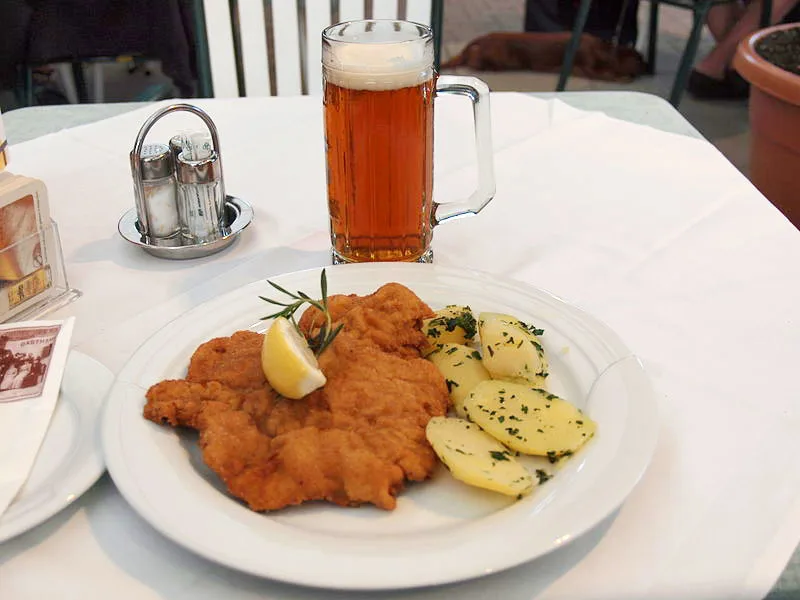 weiner schnitzel breaded pork cutlet with potatoes served on a plate on a white tablecloth with a stein of beer in the background in austria