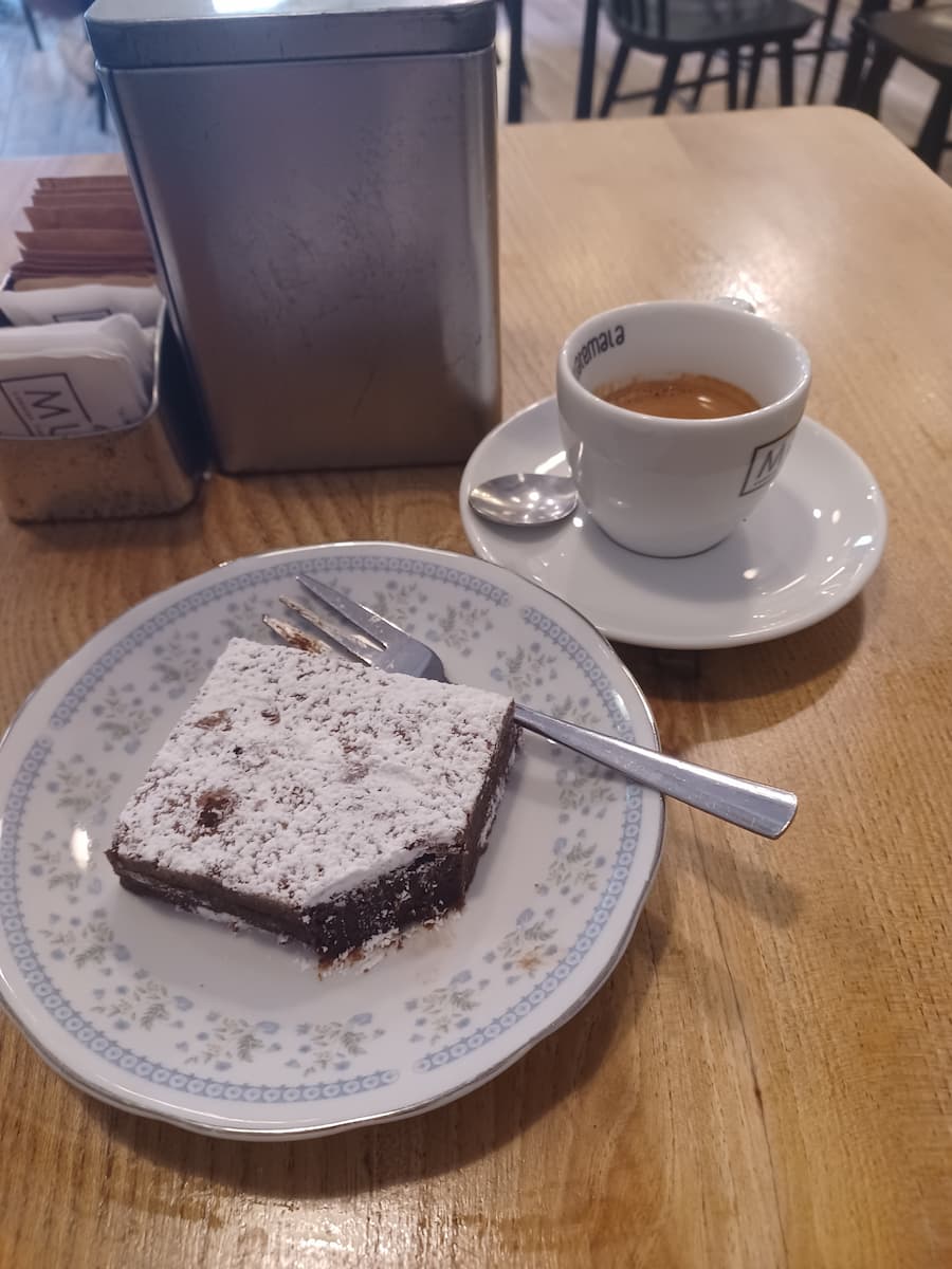 a chocolate brownie on a blue plate with a fork next to an espresso coffee at mug coffee shop trieste italy
