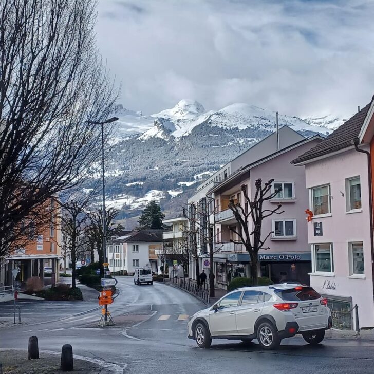 a car on a road with the alps mountains in the background in vaduz liechtenstein