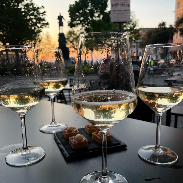 four glasses of white wine on a table outside bar sissi in trieste italy with trees in the background