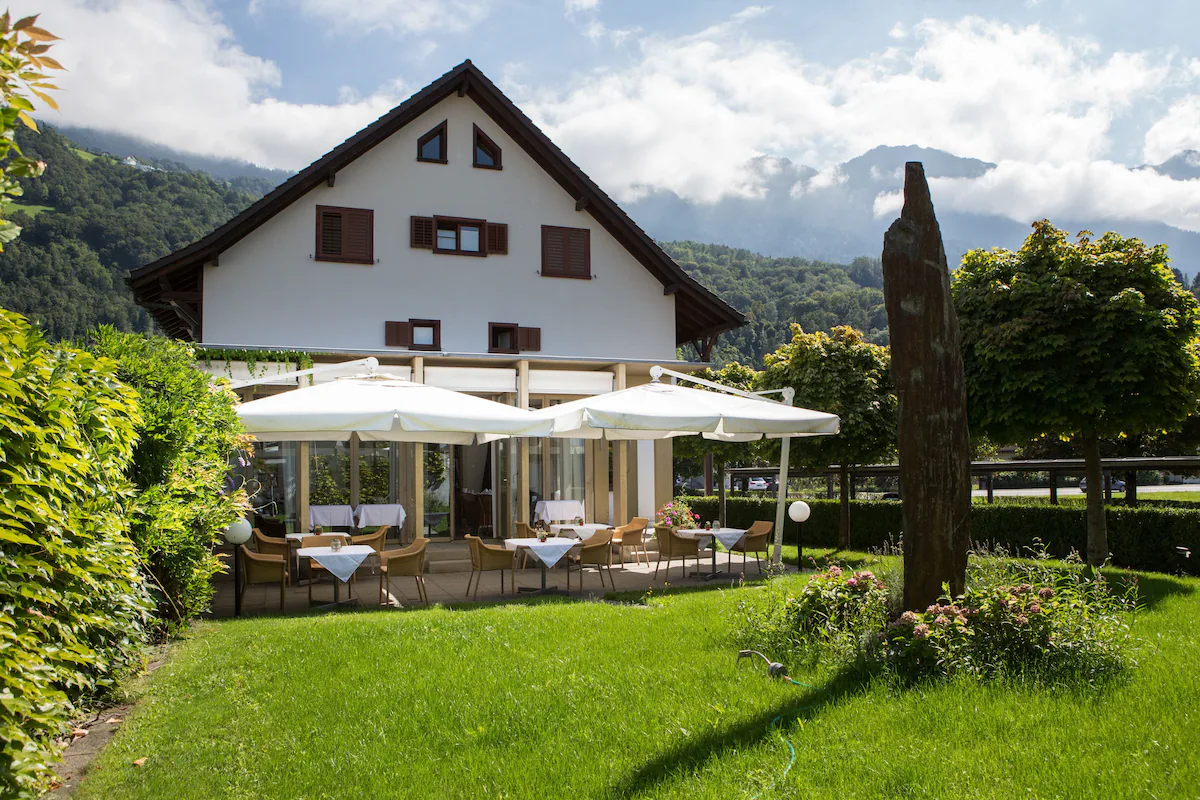 the hotel schatzmann with a patio and garden in the foreground in triesen liechtenstein