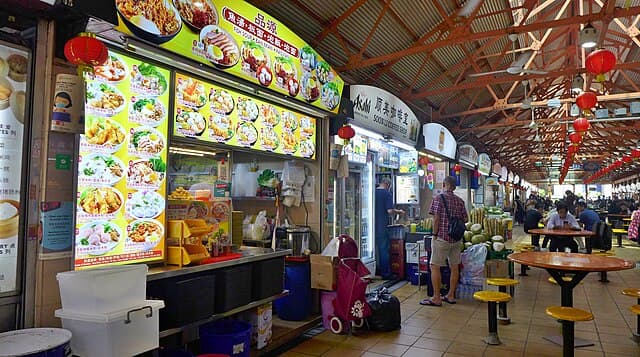 Hawker stalls lined up inside Maxwell Food Centre with tables in the middle