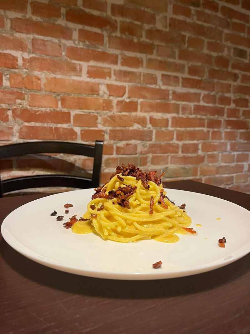 spaghetti carbonara on a white plate on a brown table with an exposed brick wall in the background at salsapiraglia italian restaurant in trieste italy