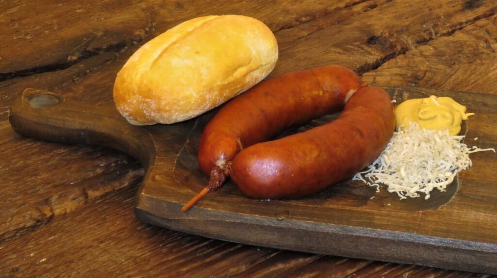 carniolan sausages are traditional slovenian foods served seen on a wooden board with a bread roll