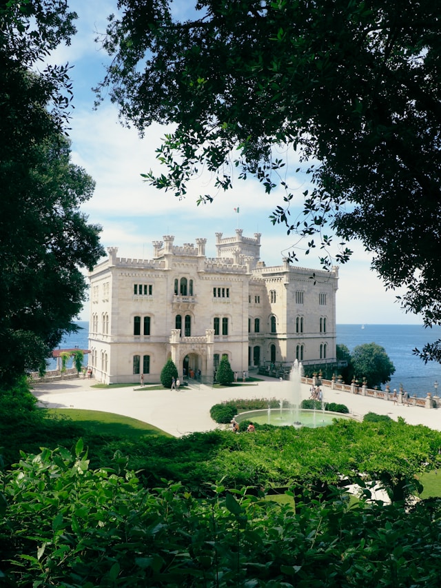 miramare castle is a large clifftop building hidden behind trees near trieste italy
