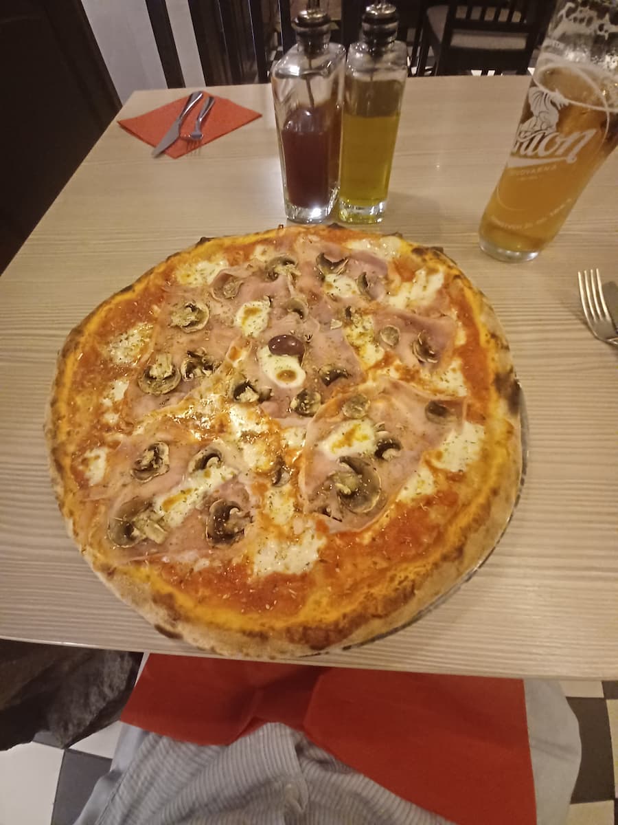 a ham and mushroom pizza on a wooden table with a glass of beer at pikasta restaurant in ljubljana slovenia