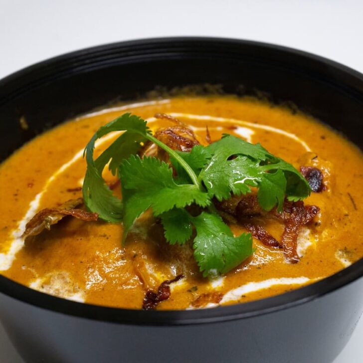 chicken makhani butter chicken curry in a black bowl with green leaves on top from zaika indian restaurant ljubljana slovenia