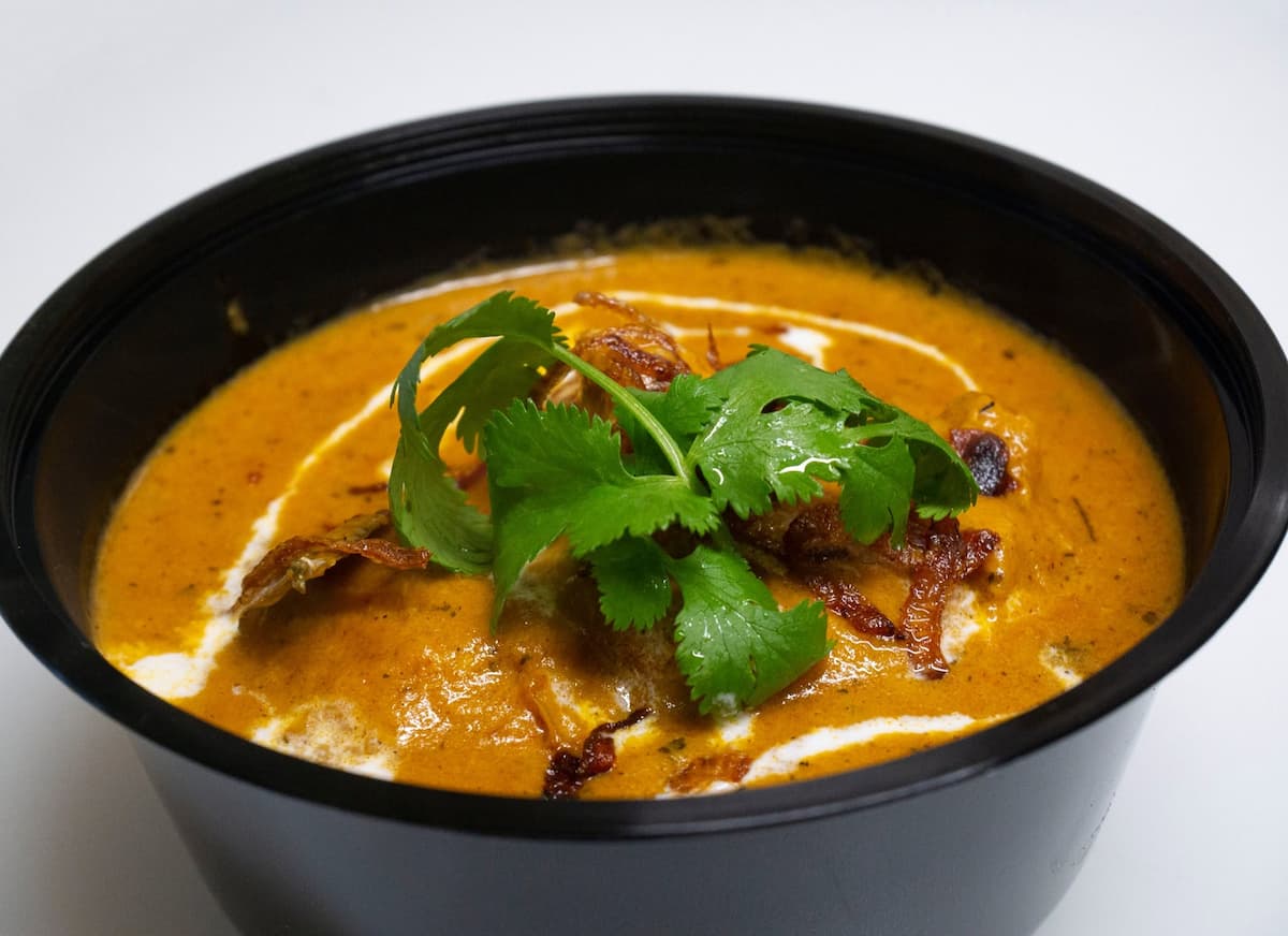 chicken makhani butter chicken curry in a black bowl with green leaves on top from zaika indian restaurant ljubljana slovenia