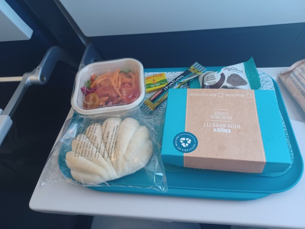 a meal tray on an airplane with a bread roll salad meal box and irish chocolate