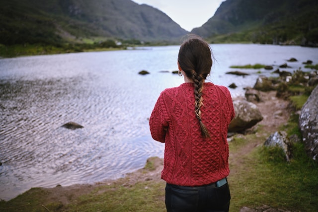 a girl wearing a red aran sweater jumper looking at a loch in the aran islands ireland